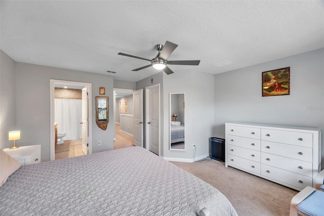 bedroom with ceiling fan, light carpet, ensuite bathroom, and a textured ceiling