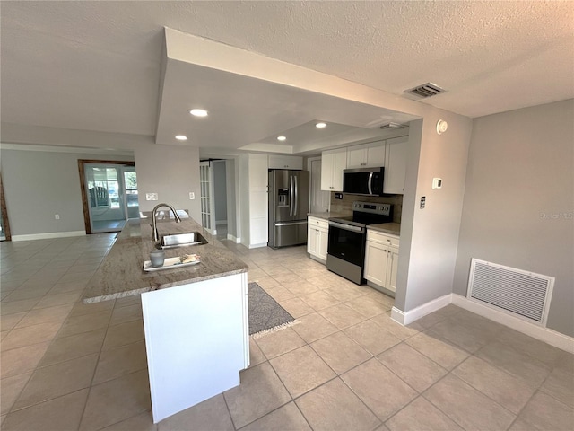 kitchen with sink, an island with sink, stainless steel appliances, light stone countertops, and white cabinets