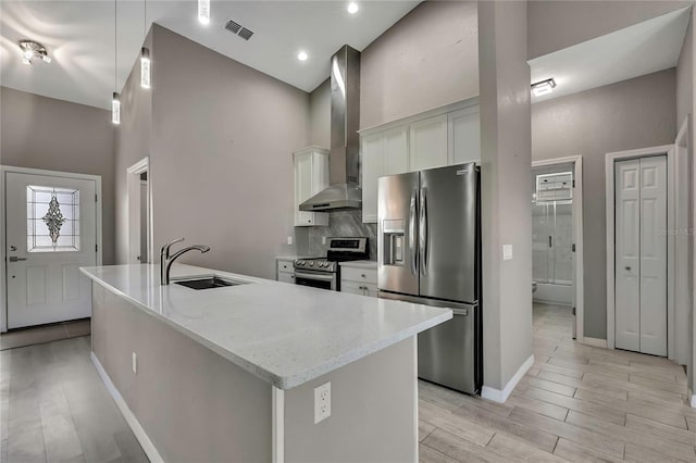 kitchen with appliances with stainless steel finishes, white cabinetry, an island with sink, sink, and wall chimney exhaust hood