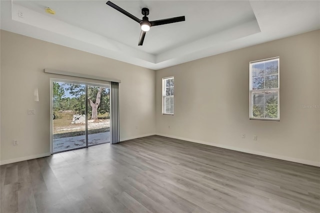 empty room with a tray ceiling, light hardwood / wood-style floors, and ceiling fan