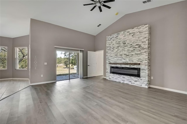 unfurnished living room featuring hardwood / wood-style floors, a stone fireplace, high vaulted ceiling, and ceiling fan