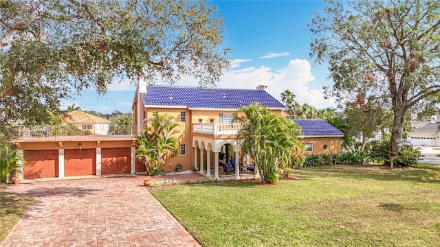 mediterranean / spanish home featuring a balcony, a garage, decorative driveway, stucco siding, and a front yard