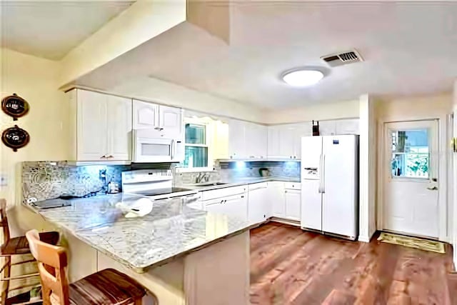 kitchen with white appliances, dark wood-type flooring, a breakfast bar, white cabinets, and kitchen peninsula