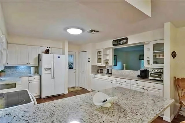 kitchen featuring white refrigerator with ice dispenser, light stone counters, white cabinets, and backsplash