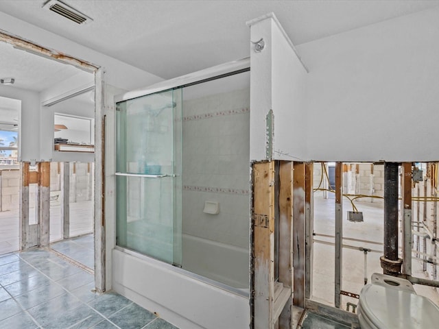 bathroom featuring tile patterned flooring, a textured ceiling, toilet, and combined bath / shower with glass door