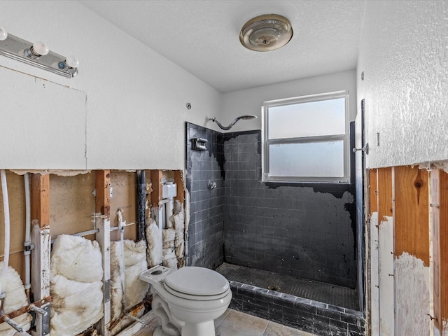 bathroom featuring tile patterned flooring, a textured ceiling, toilet, and tiled shower