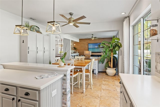 kitchen featuring a kitchen island, wood walls, decorative light fixtures, white cabinets, and ceiling fan