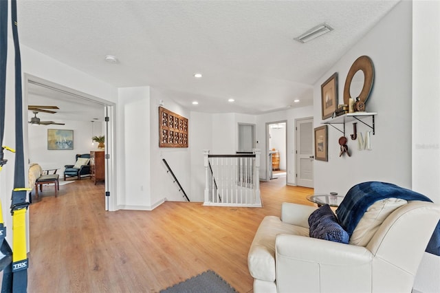 living room with ceiling fan, a textured ceiling, and light wood-type flooring