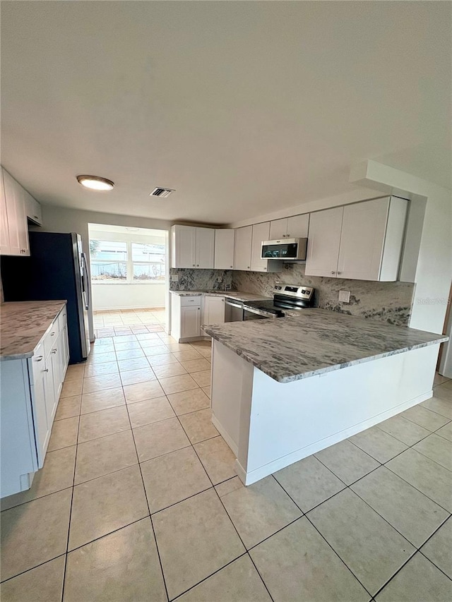 kitchen featuring white cabinetry, tasteful backsplash, light tile patterned floors, appliances with stainless steel finishes, and kitchen peninsula