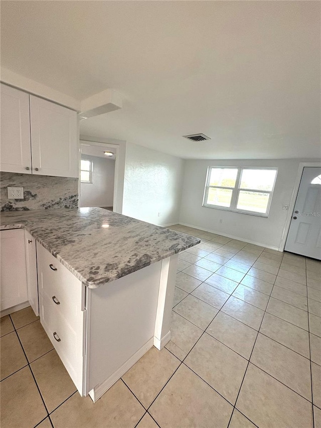 kitchen with light tile patterned floors, kitchen peninsula, white cabinets, light stone countertops, and backsplash