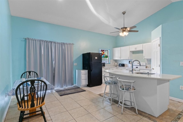 kitchen with sink, a breakfast bar area, white cabinetry, a kitchen island with sink, and black fridge