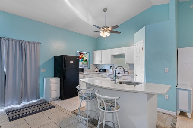 kitchen featuring a kitchen bar, sink, black fridge, a center island with sink, and white cabinets