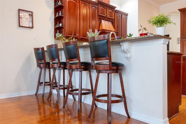 bar featuring ornamental molding, light hardwood / wood-style floors, and stone counters