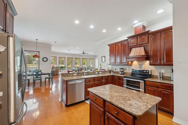 kitchen featuring sink, custom exhaust hood, decorative light fixtures, appliances with stainless steel finishes, and kitchen peninsula