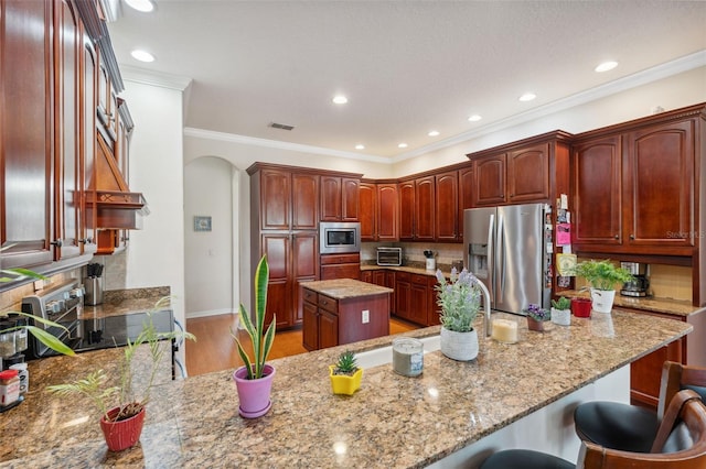 kitchen with appliances with stainless steel finishes, a breakfast bar, ornamental molding, a center island, and light stone counters