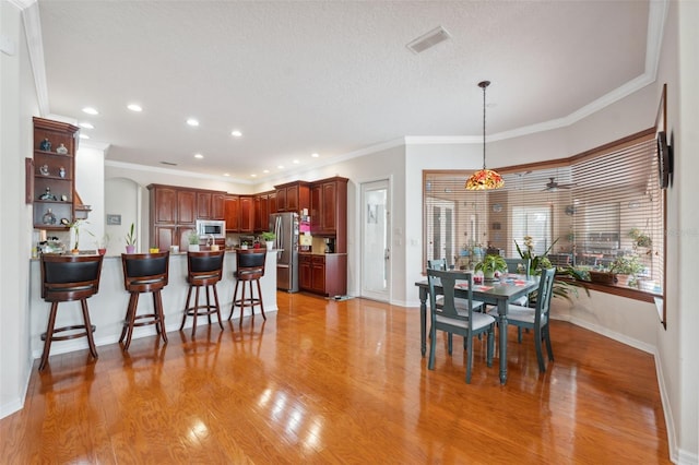 kitchen with a kitchen bar, decorative light fixtures, ornamental molding, stainless steel appliances, and light hardwood / wood-style floors