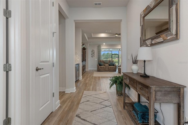 corridor with light wood finished floors, visible vents, and baseboards