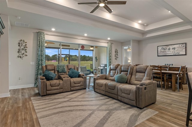 living area featuring ceiling fan, visible vents, baseboards, light wood-type flooring, and a raised ceiling