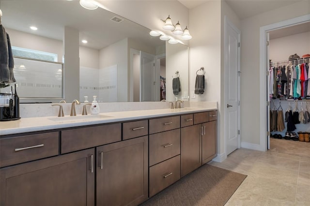 bathroom with double vanity, a spacious closet, walk in shower, and a sink