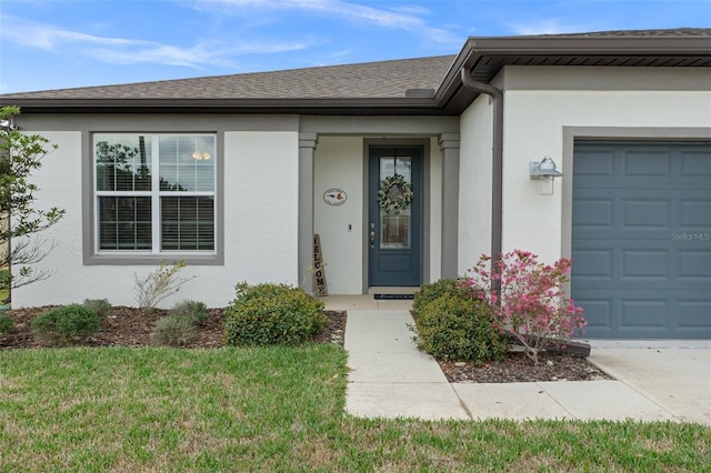 view of exterior entry featuring a garage, a shingled roof, a lawn, and stucco siding