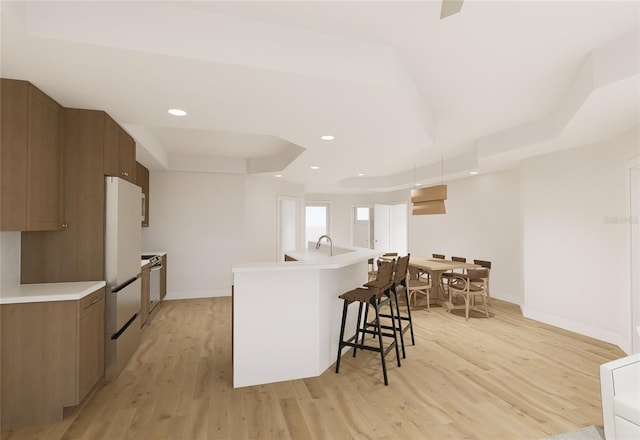 kitchen with light countertops, a tray ceiling, a kitchen bar, and light wood-style floors