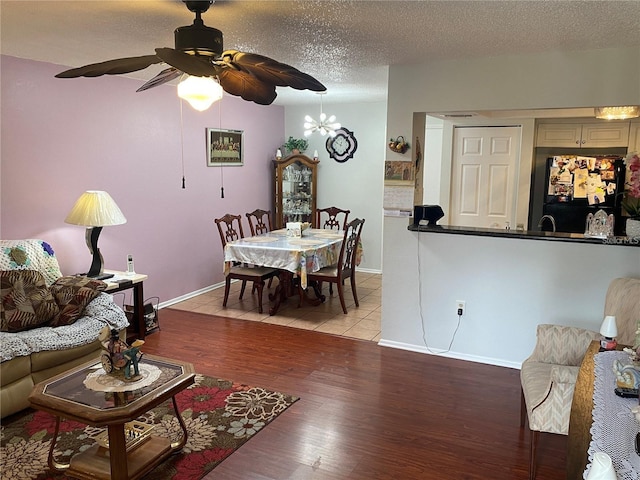 living room featuring ceiling fan with notable chandelier, a textured ceiling, and light wood-type flooring