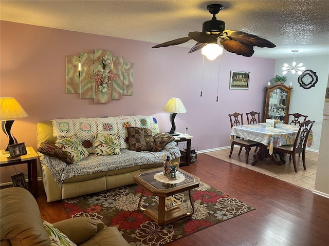 living room with ceiling fan with notable chandelier, light hardwood / wood-style floors, and a textured ceiling