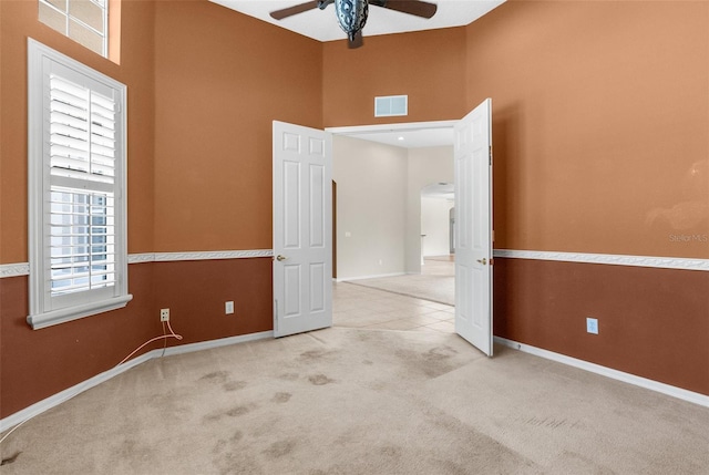 unfurnished room with light colored carpet, ceiling fan, and a high ceiling