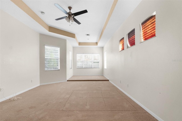 spare room with ceiling fan, a tray ceiling, and light colored carpet