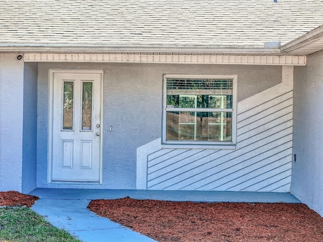 view of exterior entry with stucco siding and roof with shingles