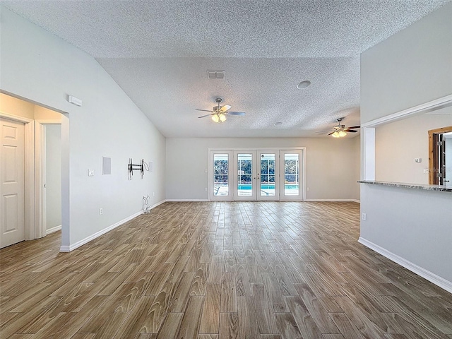 unfurnished living room with a textured ceiling, wood finished floors, visible vents, a ceiling fan, and french doors