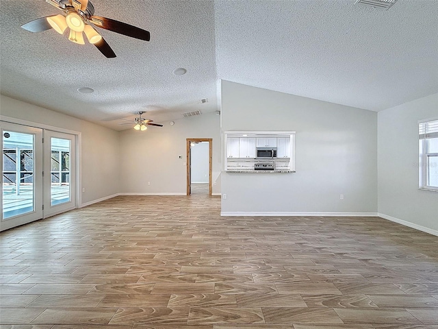 unfurnished living room with lofted ceiling, a textured ceiling, wood finished floors, visible vents, and baseboards