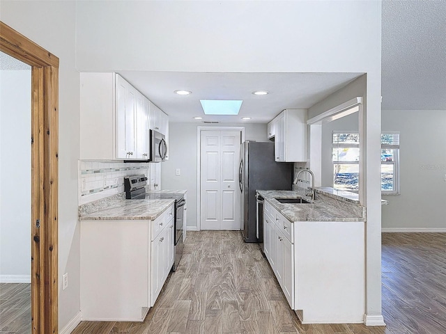 kitchen featuring baseboards, light wood-style flooring, a sink, stainless steel appliances, and backsplash