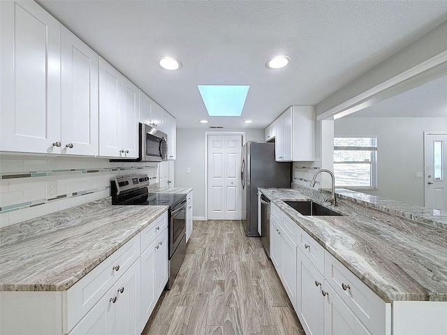 kitchen with light wood-style flooring, a sink, white cabinets, appliances with stainless steel finishes, and tasteful backsplash