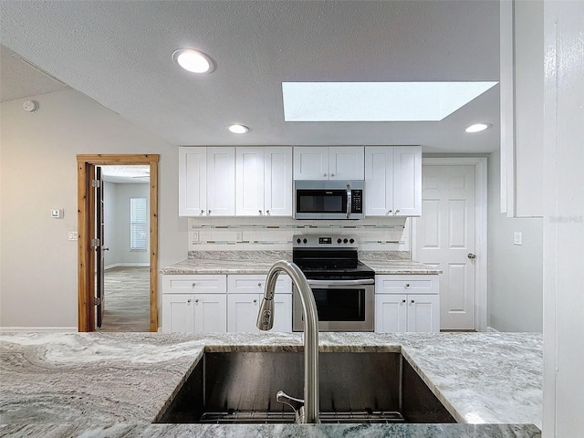 kitchen featuring tasteful backsplash, appliances with stainless steel finishes, light stone countertops, white cabinetry, and a sink