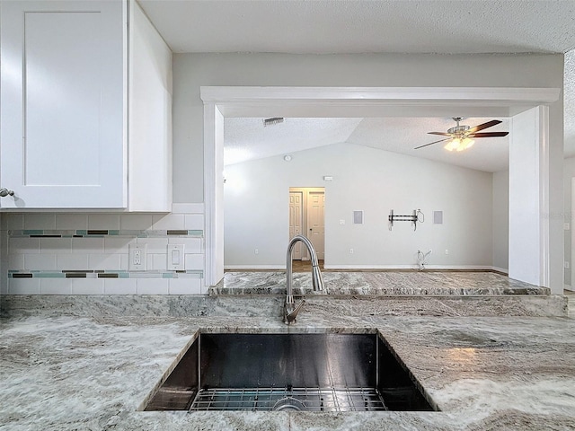 kitchen with lofted ceiling, light stone counters, a sink, white cabinetry, and tasteful backsplash