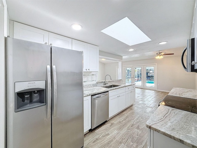 kitchen with a skylight, white cabinets, light stone countertops, stainless steel appliances, and a sink