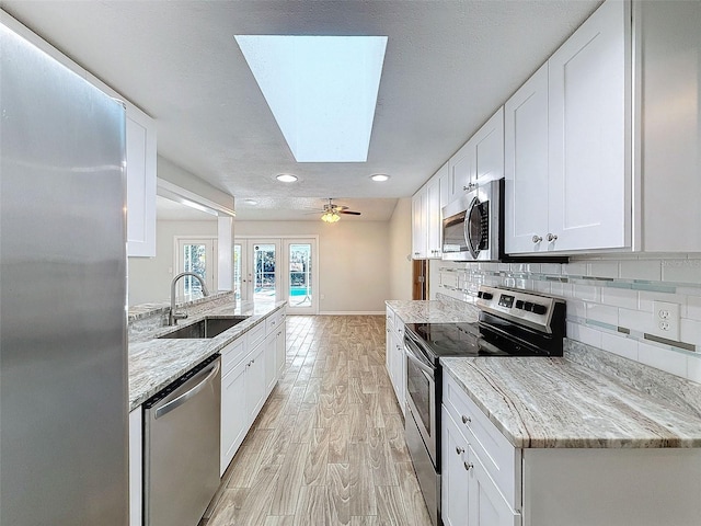 kitchen with a sink, white cabinets, appliances with stainless steel finishes, light wood finished floors, and tasteful backsplash