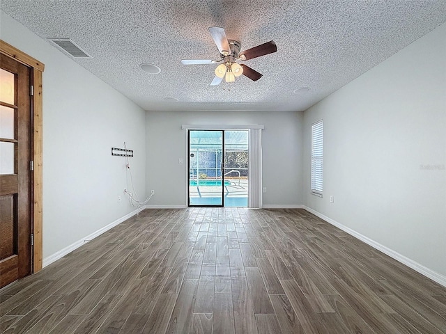 spare room featuring dark wood-style floors, baseboards, visible vents, and a textured ceiling