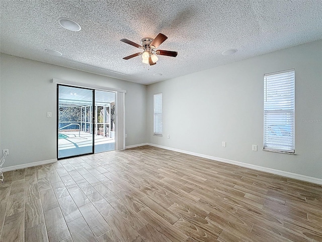 empty room featuring a textured ceiling, wood finished floors, a ceiling fan, and baseboards