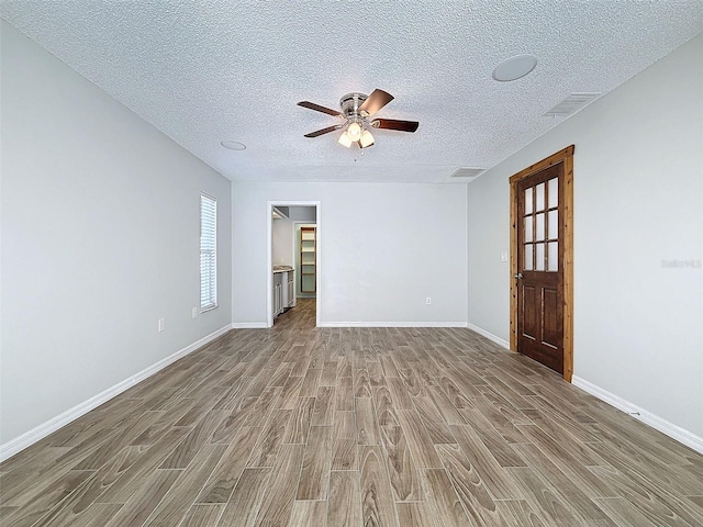 empty room featuring a textured ceiling, wood finished floors, a ceiling fan, visible vents, and baseboards