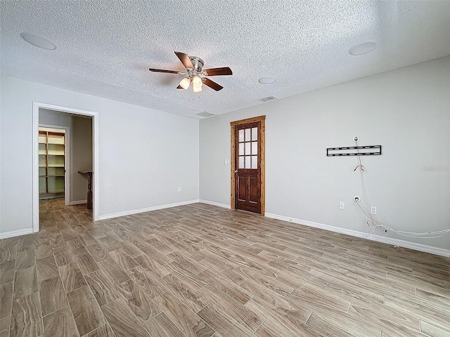 spare room featuring visible vents, light wood-style floors, ceiling fan, a textured ceiling, and baseboards