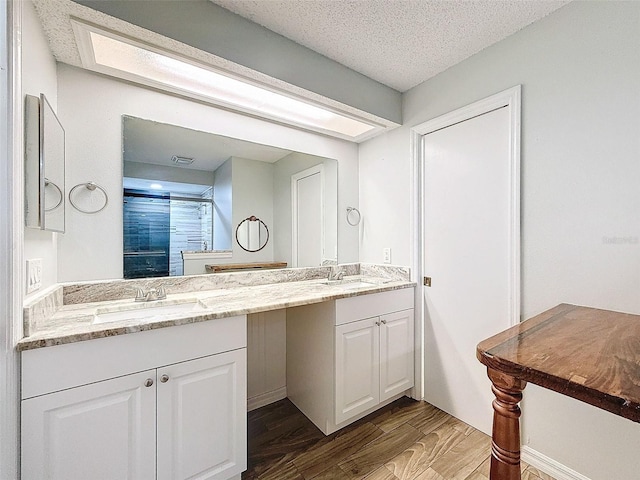 bathroom featuring a textured ceiling, double vanity, wood finished floors, and a sink