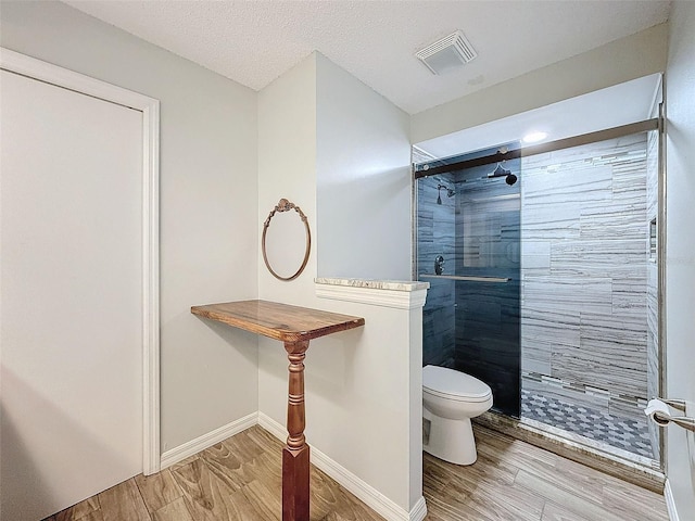 bathroom featuring toilet, visible vents, tiled shower, and wood finished floors