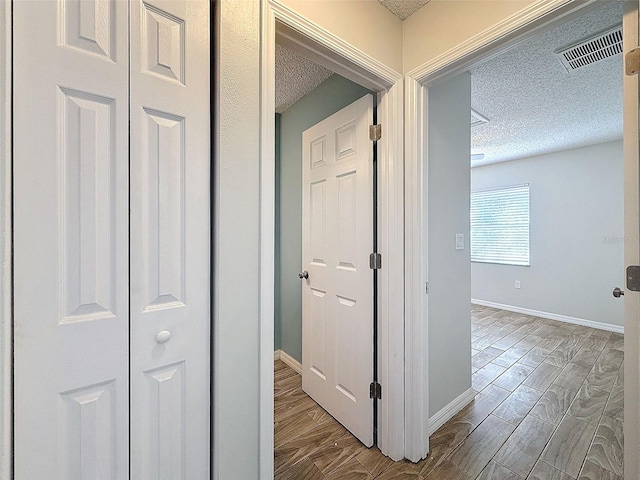 corridor with baseboards, wood tiled floor, visible vents, and a textured ceiling