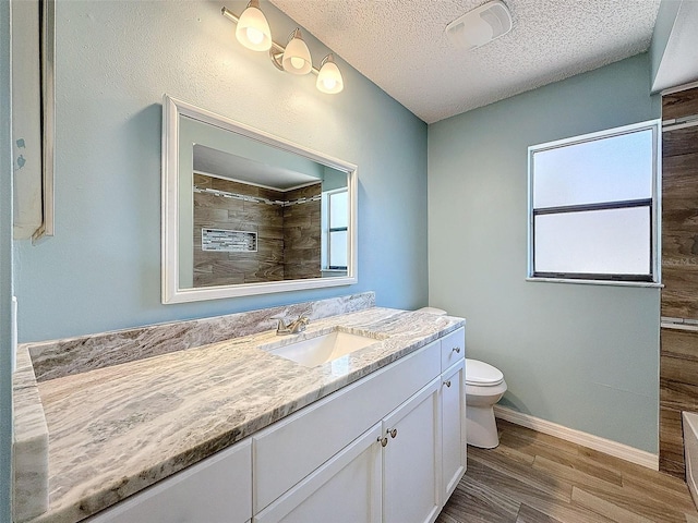 bathroom with a textured ceiling, toilet, wood finished floors, vanity, and a tile shower