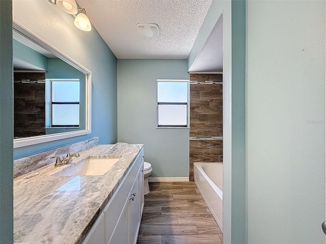 full bath featuring toilet, a textured ceiling, vanity, wood finished floors, and baseboards