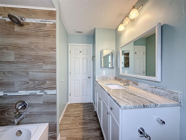 bathroom featuring visible vents, a bathing tub, wood finished floors, a textured ceiling, and vanity