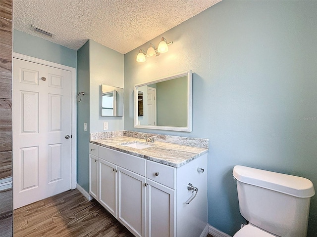 bathroom with visible vents, toilet, wood finished floors, a textured ceiling, and vanity