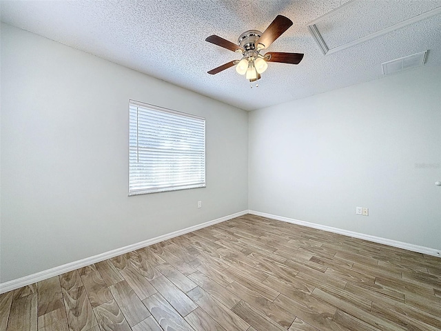 spare room with a textured ceiling, wood finished floors, visible vents, and baseboards